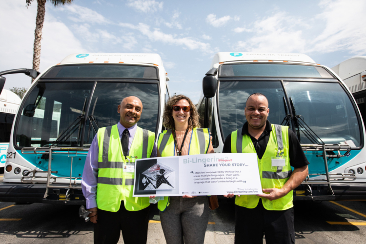 Britt Card from Transit of City of Pasadena stands in between two bus drivers holding a “Bi-Lingering” placard with a quote written by a Bi-Linger letter sender.